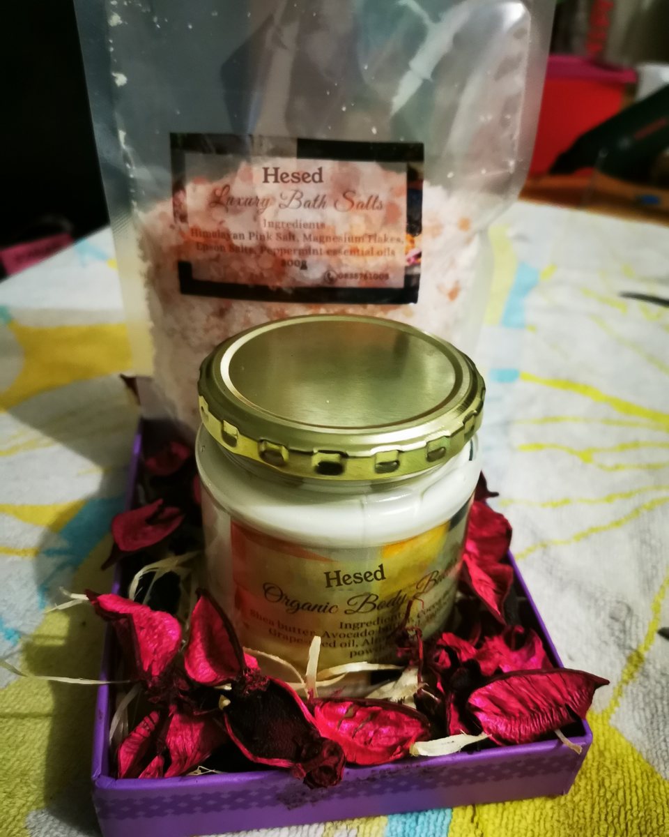 Gift box with a bag of bath salts and a jar of body butter on dried rose petals