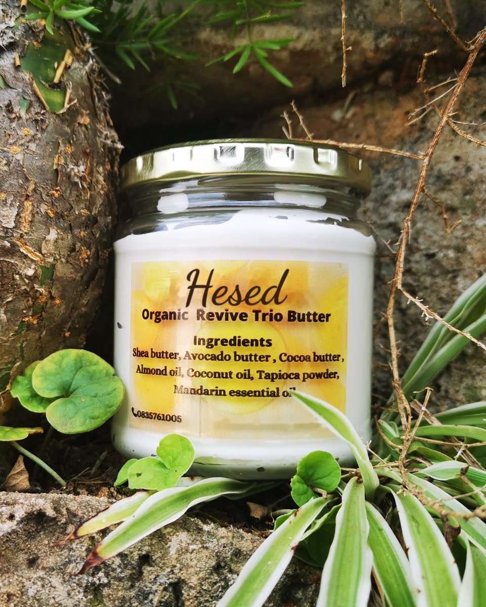 Jar of Organic Revive Trio Butter with its yellow label, among plants on a stone wall