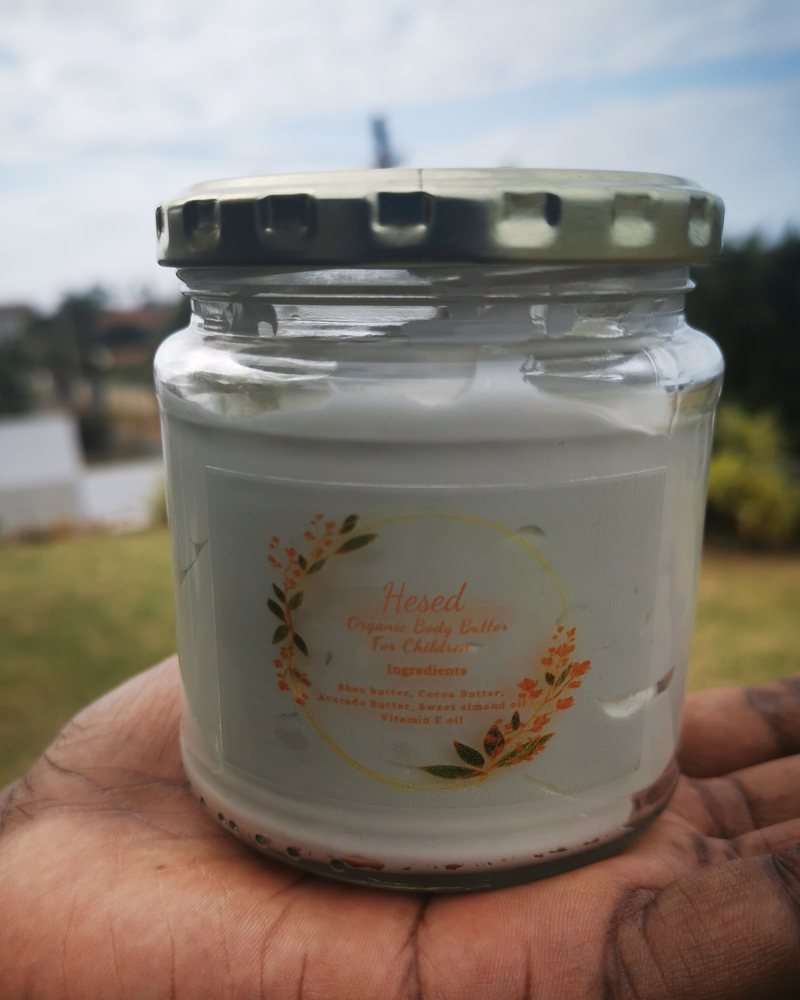 A jar of Hesed children's body butter held in the palm of a hand